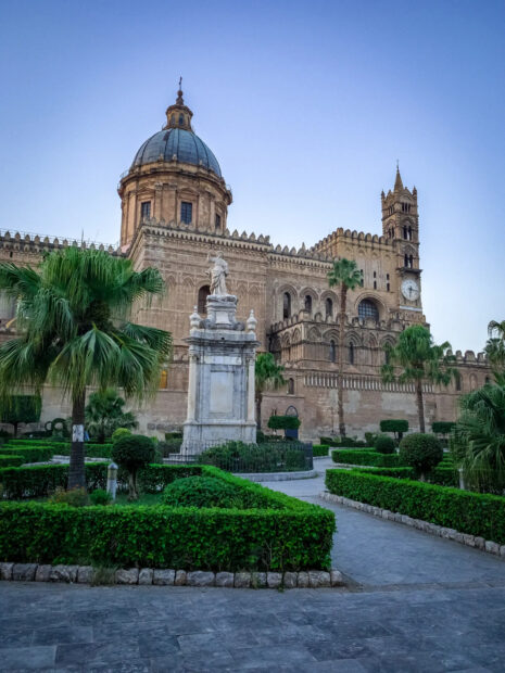 Historical Palermo architecture with lush garden and statue in foreground