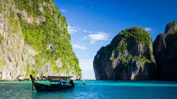 A traditional boat floating near the limestone cliffs of Phi Phi in crystal clear blue water