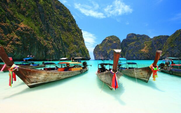 Traditional wooden boats docked at Phi Phi islands with clear turquoise water and limestone cliffs