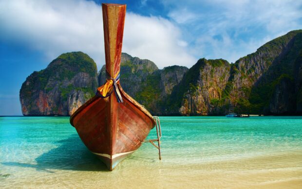 Traditional longtail boat in Phi Phi turquoise water and rocky cliffs