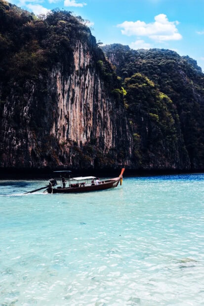 Traditional boat sailing near tall cliffs in Phi Phi with clear blue water