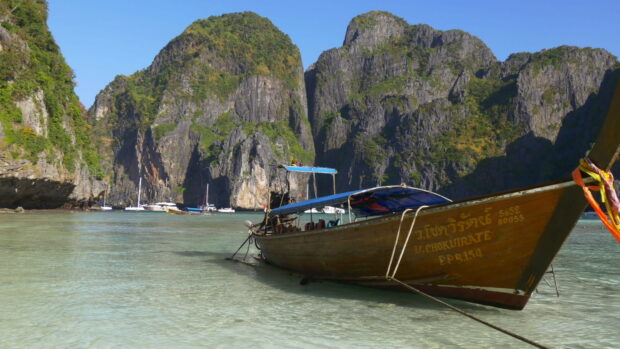 Traditional wooden boat floating near limestone cliffs at Phi Phi island