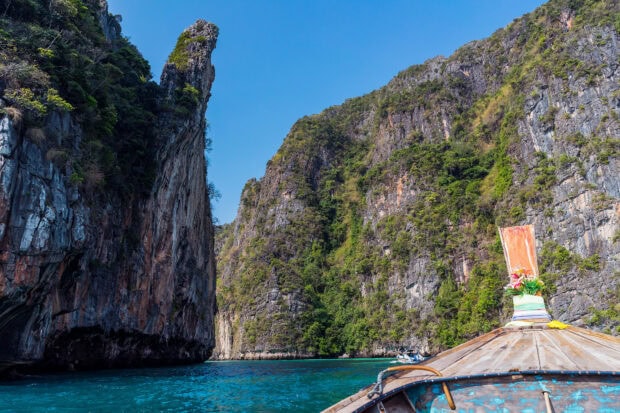A traditional boat sailing through turquoise waters near rocky cliffs in Phi Phi