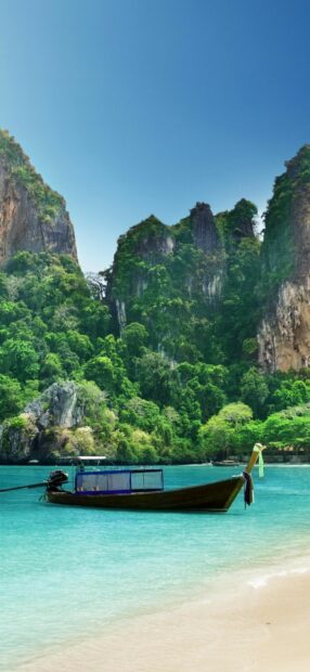 Traditional boat floating on clear turquoise water near green cliffs in Phi Phi