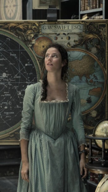 A woman wearing a vintage dress stands in front of an antique navigation chart in a historical setting
