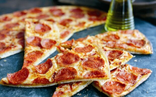 Delicious pepperoni pizza slices on a baking tray with olive oil in the background