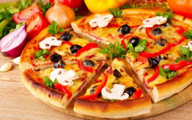 A delicious pizza topped with mushrooms olives red peppers and fresh herbs on a wooden table