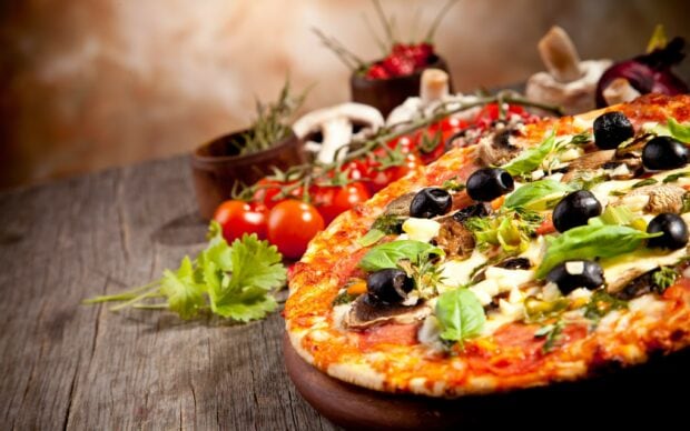 A delicious pizza topped with olives mushrooms and fresh herbs on a wooden table