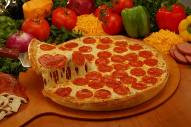 A delicious pizza topped with pepperoni surrounded by fresh vegetables and cheese on a wooden surface
