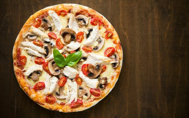 A delicious pizza with chicken mushroom and tomato toppings on a wooden surface