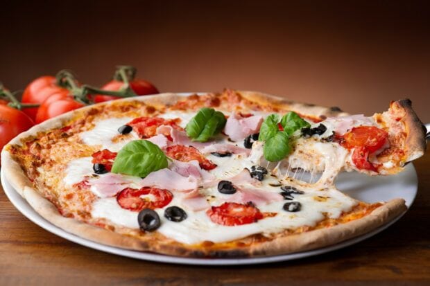 A delicious pizza with ham tomato olives and fresh basil on a white plate