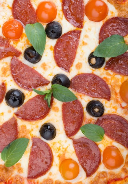 Close up of pizza with pepperoni black olives cherry tomatoes and basil leaves on melted cheese