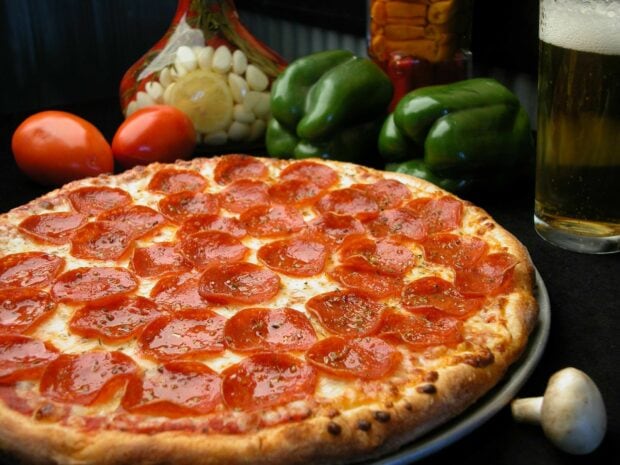 A pepperoni pizza served with fresh green peppers tomatoes and garlic on a dark table