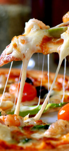 A close up of a slice of pizza with melted cheese stretching and fresh toppings