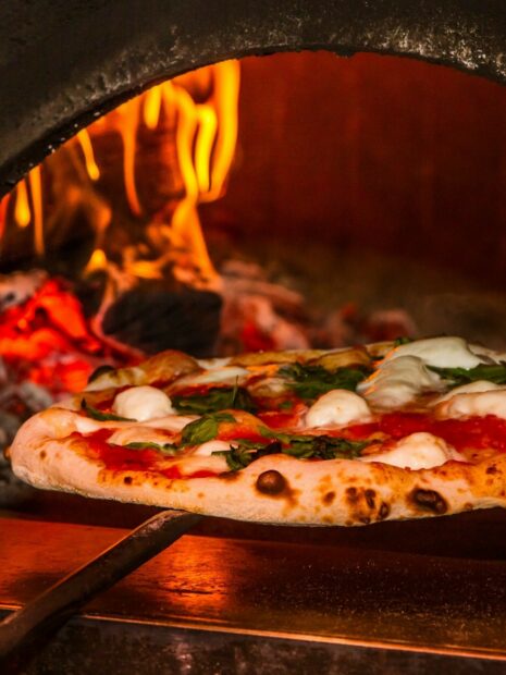 Fresh pizza with basil and cheese baking in a wood fired oven