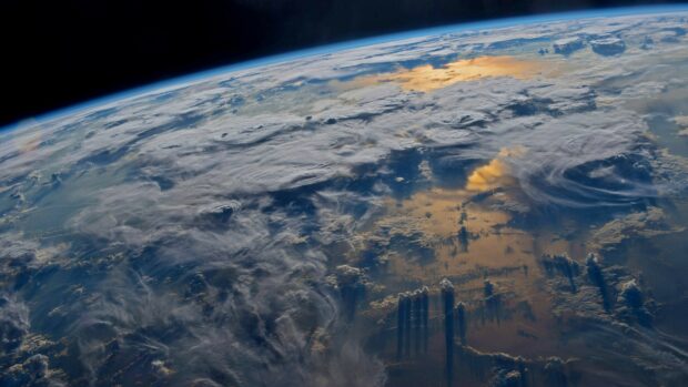 Earth visible from space with swirling clouds and sunlight reflections on the surface