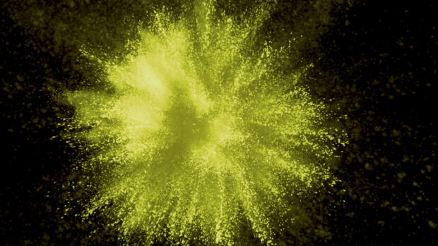 Yellow powder explosion spreading on a black background with vibrant particles