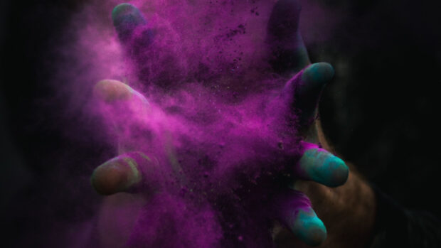 Hands releasing vibrant purple powder in dark settings with powder