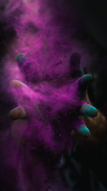 Purple powder bursting from hands in dark setting