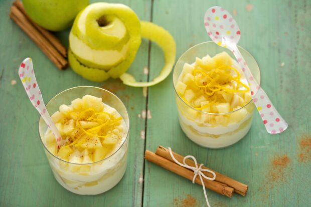 Two creamy pudding desserts topped with diced apple and lemon zest on a wooden table