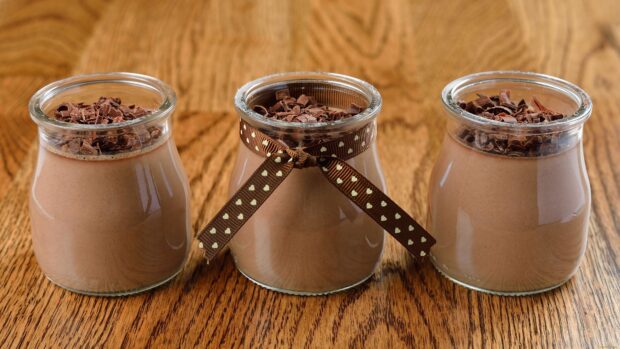 Three jars of chocolate pudding topped with chocolate shavings on a wooden surface
