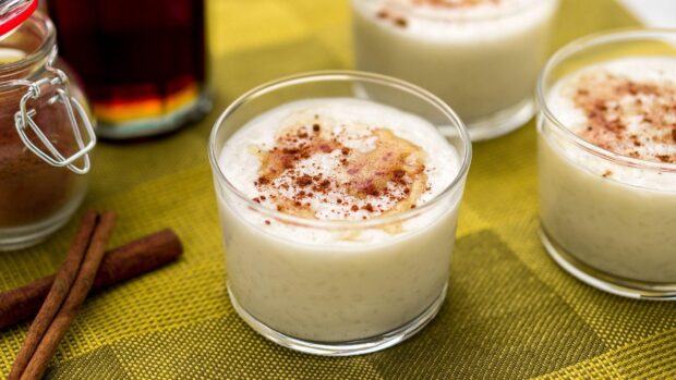 Creamy pudding topped with cinnamon and syrup in a glass cup on a green surface