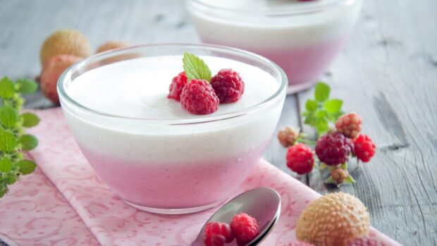 A glass bowl of creamy pudding topped with fresh raspberries and a mint leaf