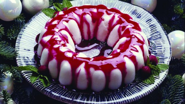 A pudding dessert with berry sauce drizzled on top and fresh mint leaves on a glass plate