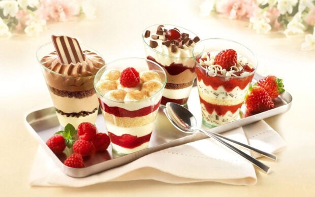 A variety of pudding desserts with raspberries and strawberries on a tray