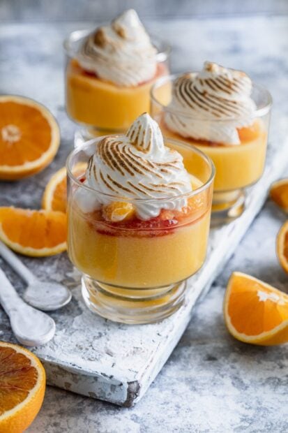 A close up of delicious pudding topped with whipped cream and orange slices in clear glasses