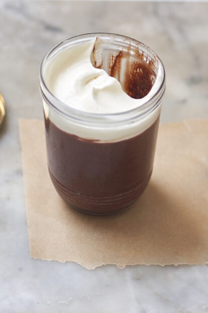 Chocolate pudding with whipped cream topping in a glass jar on a marble surface