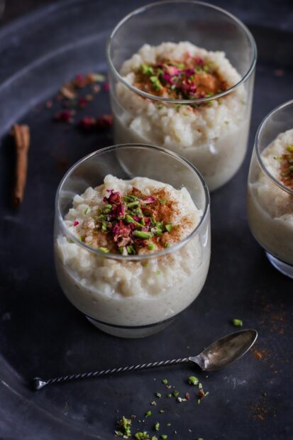 Creamy pudding topped with chopped pistachios and rose petals in clear glasses