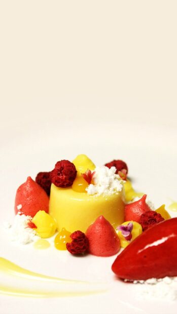 A colorful pudding dessert with raspberries and red and yellow cream dollops on a white plate