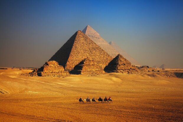 The ancient pyramids of Giza standing tall in the desert with a caravan of camels passing by