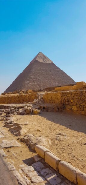Ancient pyramids of Giza surrounded by desert and stone ruins under a clear blue sky