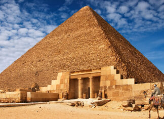 The Great Pyramid of Giza with a camel rider in the foreground under a blue sky