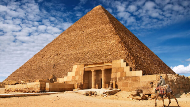 The Great Pyramid of Giza with a camel rider in the foreground under a blue sky