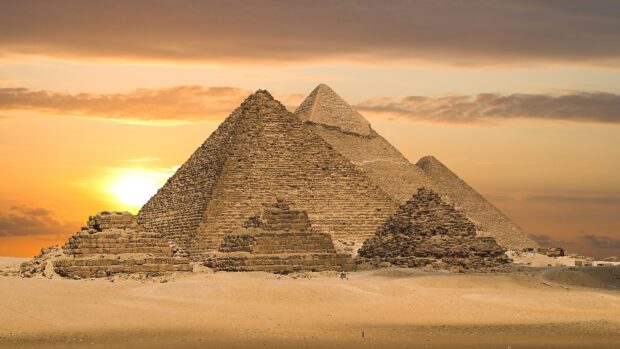 The Pyramids Of Giza stand majestically under a golden sunset sky in the desert