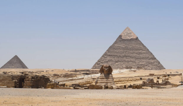 The sphinx and pyramids of Giza standing in the desert under clear blue sky
