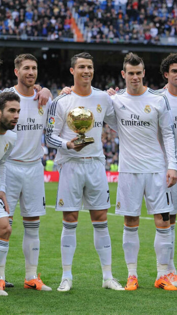 Cristiano Ronaldo holding a golden trophy with Real Madrid Cf teammates on the field