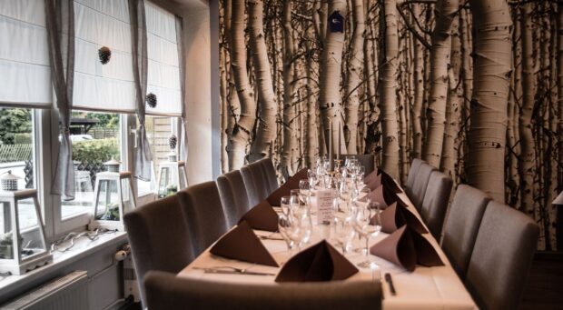 A restaurant dining area with a long table set for a meal and a birch tree themed wall d&eacute;cor