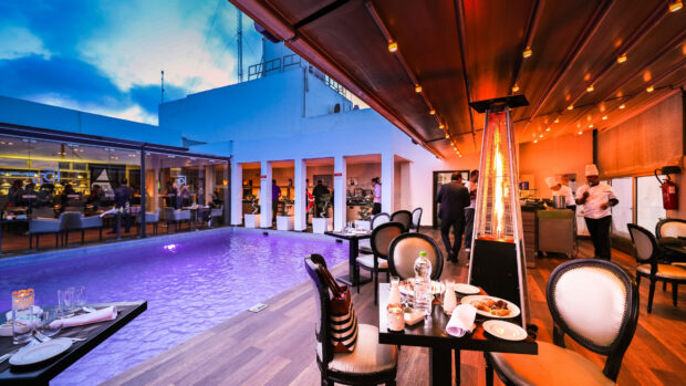 Outdoor restaurant setting with pool and diners enjoying evening meal in warm lighting