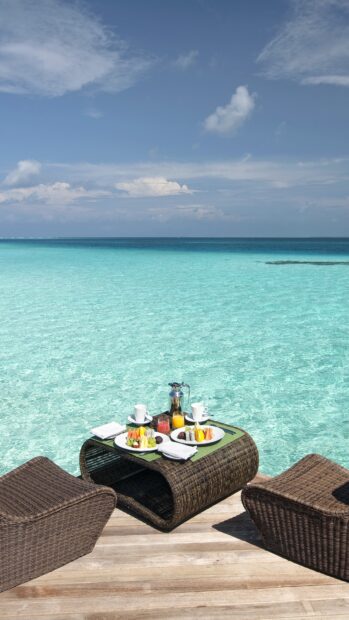 Tropical restaurant table with fresh fruit and drinks by the clear ocean water