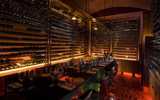 A wine cellar room in a restaurant filled with wine racks and tables set for dining with glasses and plates