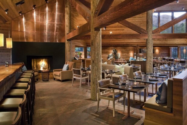 A cozy restaurant interior featuring wooden beams and furniture with a warm fireplace