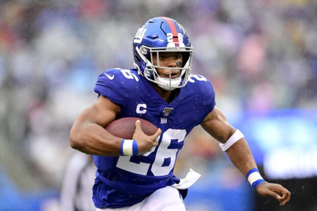 Saquon Barkley running with the football during a rainy game in a blue uniform