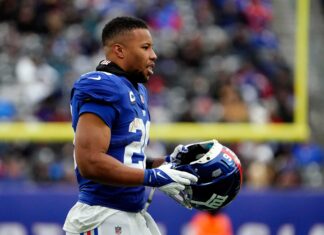 Saquon Barkley holding a football helmet on the field during a game