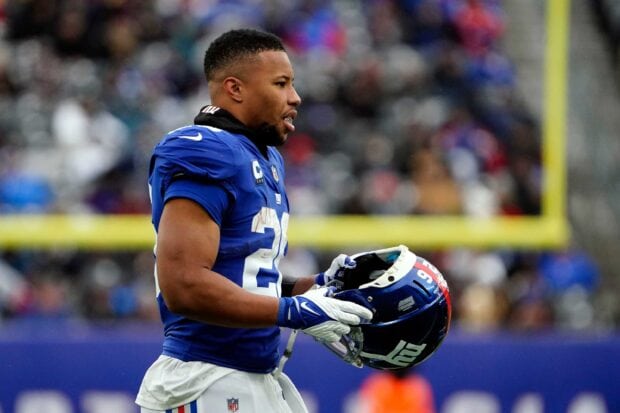 Saquon Barkley holding a football helmet on the field during a game