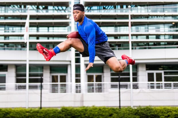 Saquon Barkley jumping in midair while holding a football during practice session