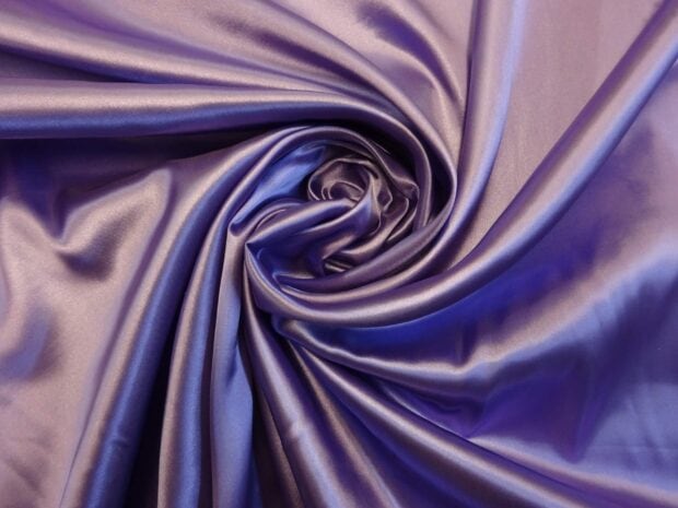 Close up of satin fabric texture with smooth folds and purple color silk feeling